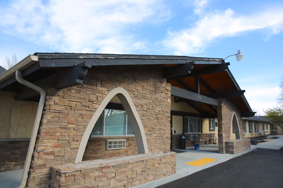 Stone-faced front entrance of a single-story care facility with arched openings and a covered walkway.