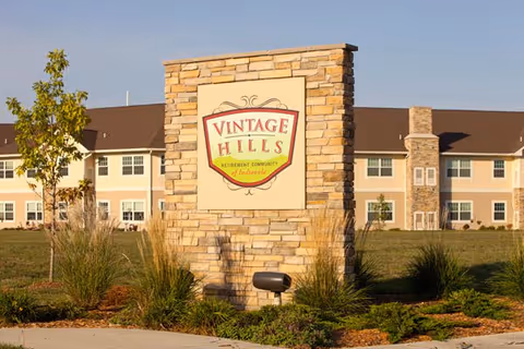 A stone monument sign reading 'Vintage Hills' stands in landscaped lawn in front of a two-story retirement community building.