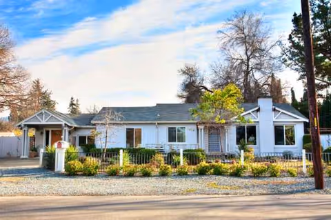 A single-story white care home with a manicured front yard and low fence.