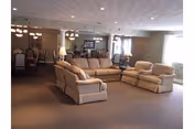 Large communal lounge in a senior facility with sofas, armchairs, and dining tables under chandeliers.