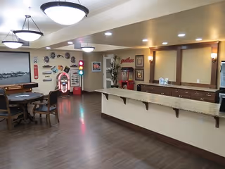 Communal activity room with a long serving counter, round table and chairs, and a jukebox and game machines along the back wall.