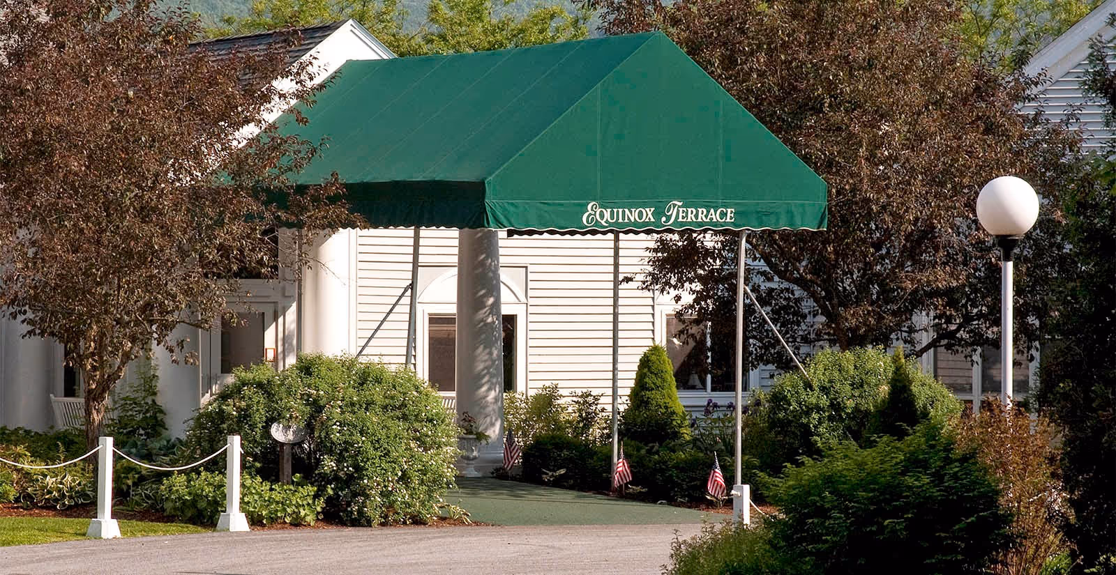 Front entrance of Equinox Terrace with a green awning over white columns and landscaped shrubs.