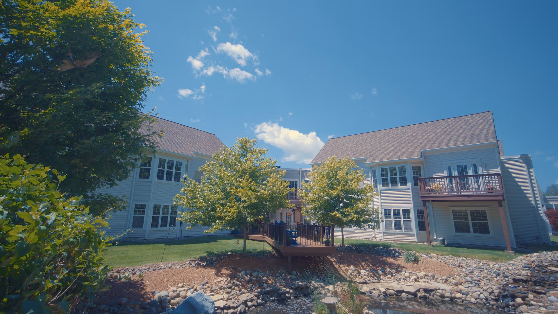 Exterior view of Autumn House Bloomfield Hills featuring a landscaped area with trees, a wooden deck, and a clear blue sky.