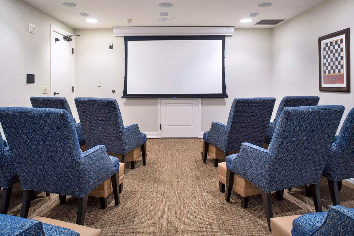 Small screening room with rows of blue upholstered chairs facing a white projection screen.
