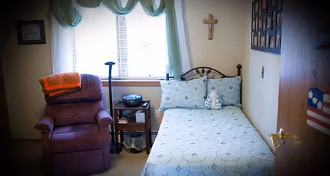 Small bedroom with a single bed, purple recliner, and window with green curtains.