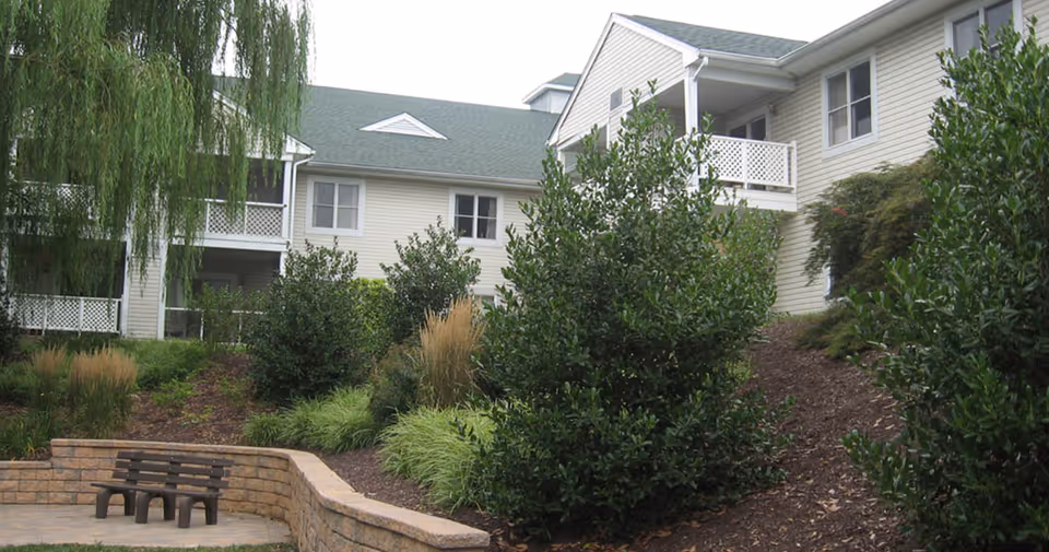 Landscaped courtyard with shrubs, a bench, and the exterior of a multi-unit building with balconies.