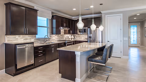 Modern kitchen with dark cabinets, a central island with stools, stainless steel appliances and pendant lights.