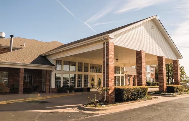 Entrance of a brick senior living facility with a covered porte-cochère supported by brick columns and large windows.