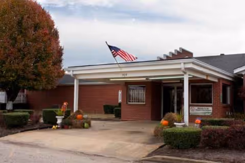 Front view of Adamsville Healthcare and Rehabilitation Center with flag and autumn decorations.