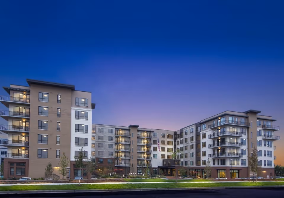Exterior view of a modern multi-story senior living facility building named Carillon at Belleview Station during twilight, with lights on inside and a clear sky above.