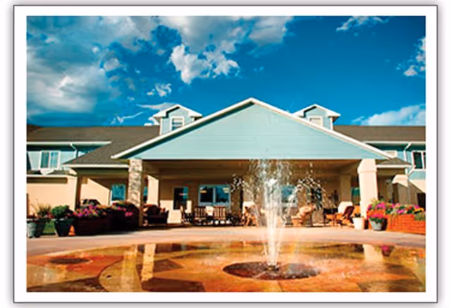 Front entrance of a senior living building with a circular fountain and seating under a covered portico.