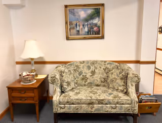 Floral-pattern loveseat with a side table and lamp beneath a framed painting on a white wall.