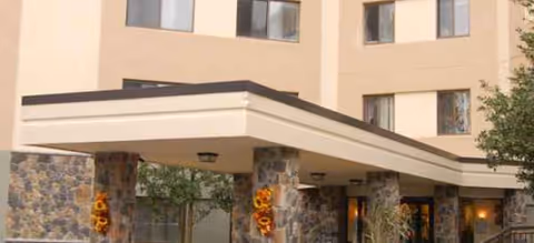Beige multi-story senior living entrance with stone pillars and sunflowers decorating the front.
