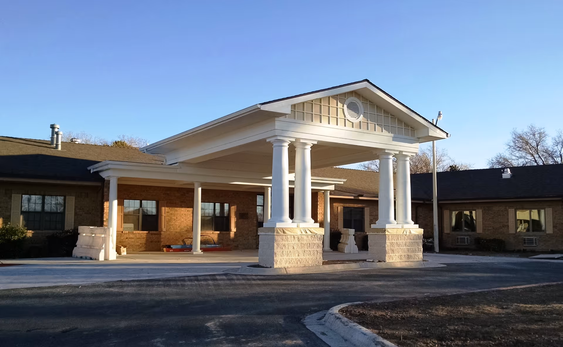 Front exterior view of Memorial Nursing & Rehabilitation Center showing a covered entrance with white columns and a brick building under a clear blue sky.
