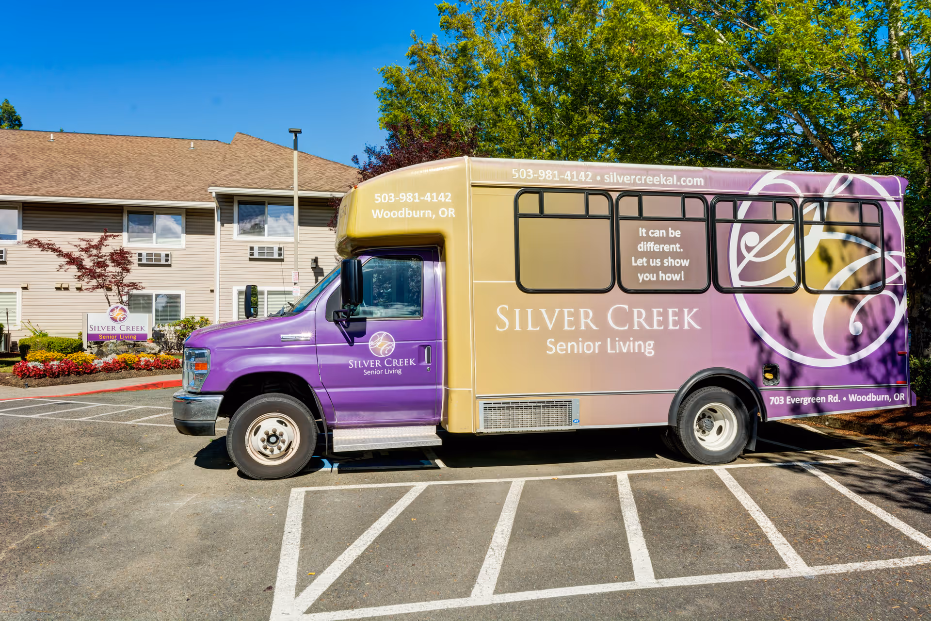 A purple and gold Silver Creek Senior Living shuttle bus parked outside the facility in front of the building and landscaped entrance.