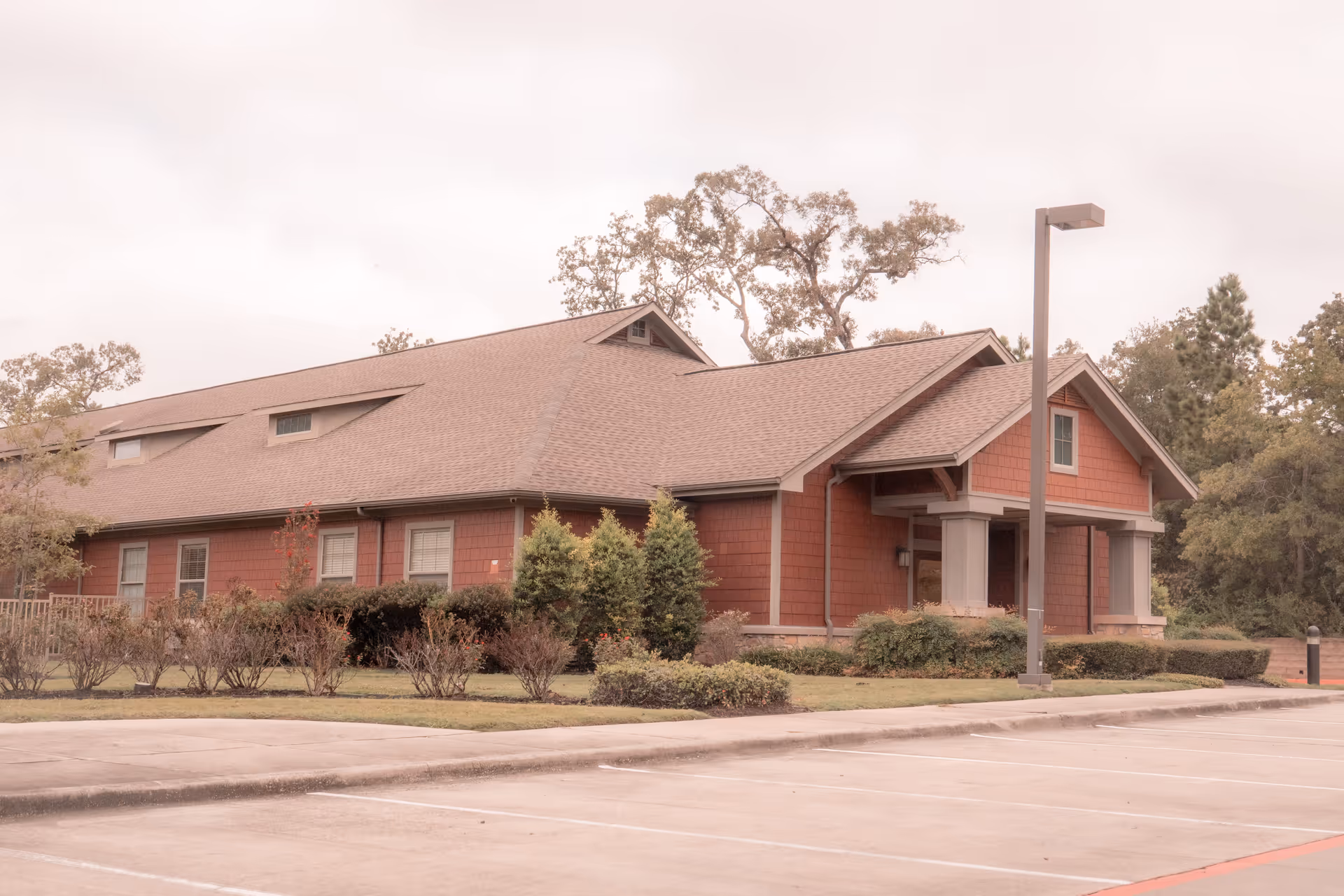 Single-story red building with a peaked roof, covered entrance, landscaping and an empty parking lot in front.