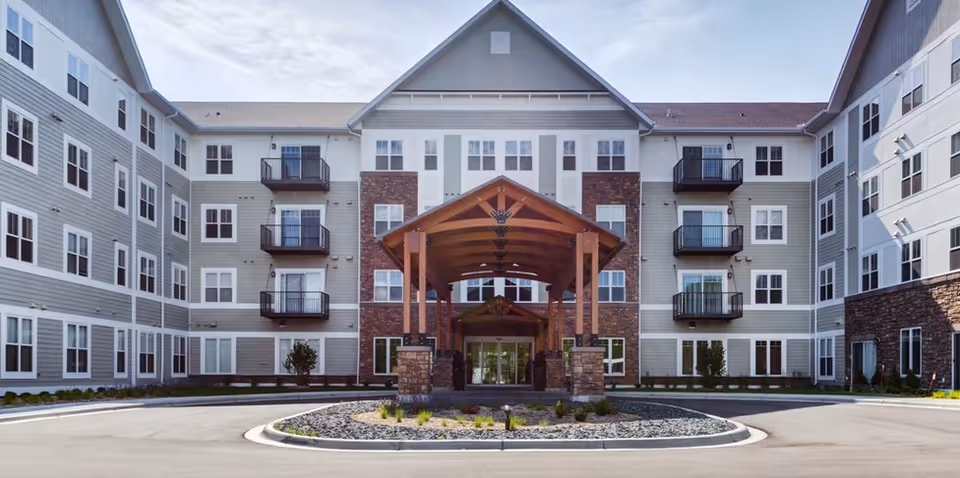 Exterior front of a multi-story senior living building with a wooden porte-cochere and circular driveway.