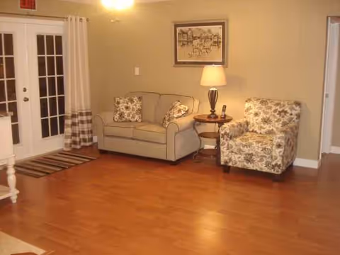 Cozy living room with beige sofa, floral armchair, side table, lamp, and framed art.