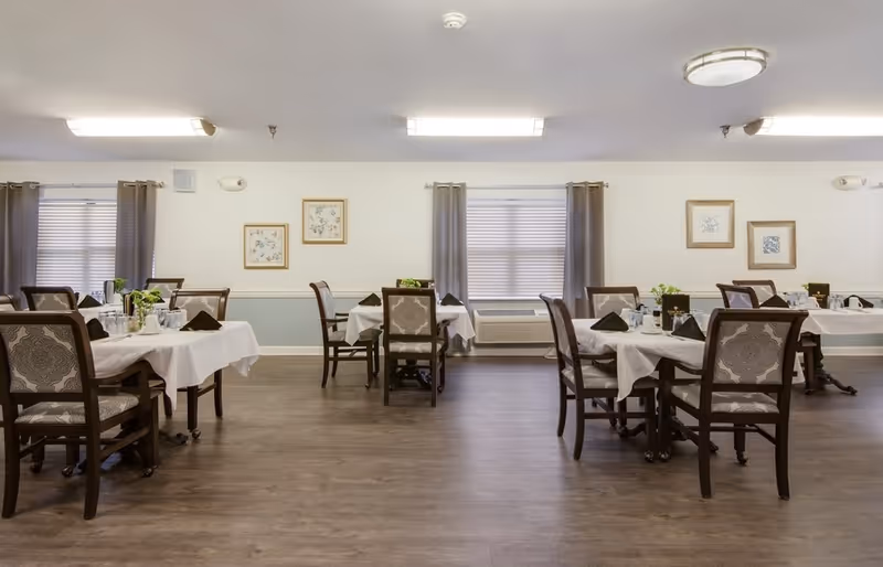 Spacious dining room with multiple tables set with white tablecloths and chairs under soft lighting.