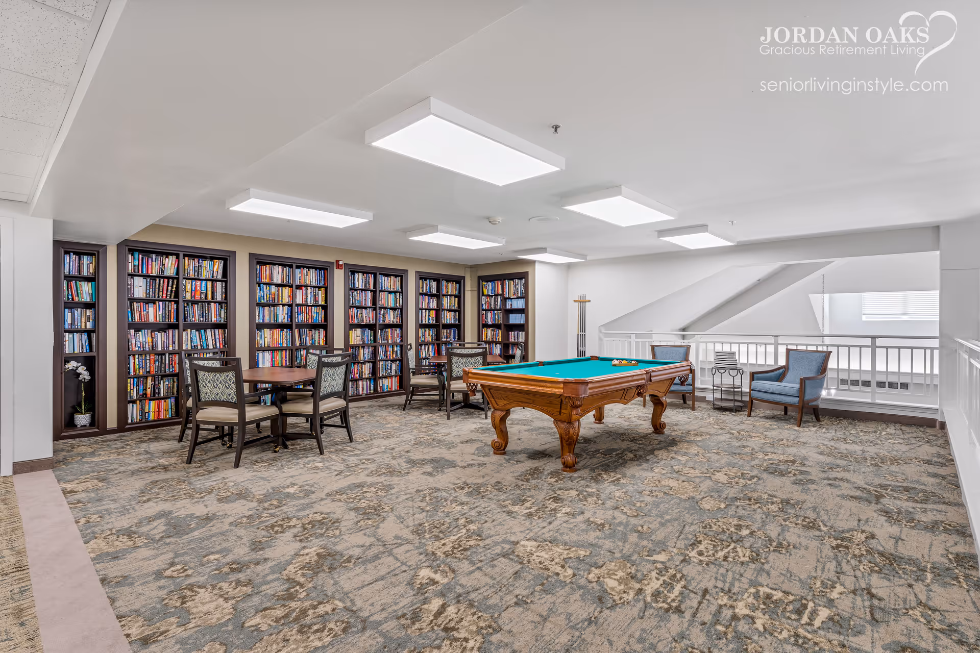 A senior living community game room with a pool table, bookshelves, and seating.