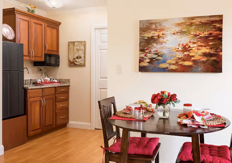 Small dining area with a round table set for a meal and a kitchenette with wooden cabinets, a refrigerator, and microwave.