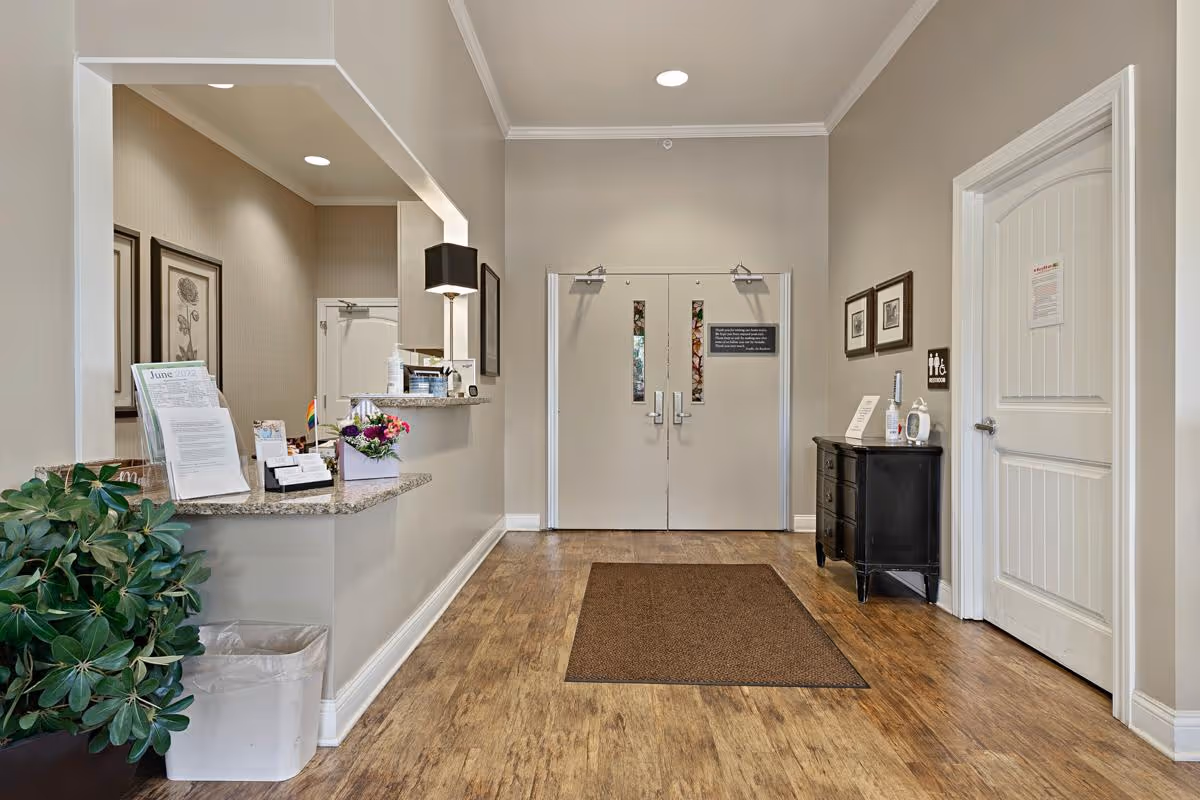 Reception area with a check-in counter to the left, double entry doors ahead, and a small table and plant on the right.
