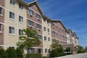 Exterior view of a multi-story senior living building with beige and brown siding and blue sky.