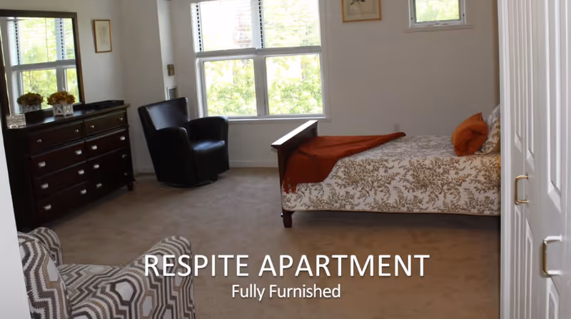 Furnished bedroom with a single bed, dresser, two chairs and large windows, shown with overlaid text reading 'RESPITE APARTMENT Fully Furnished'.