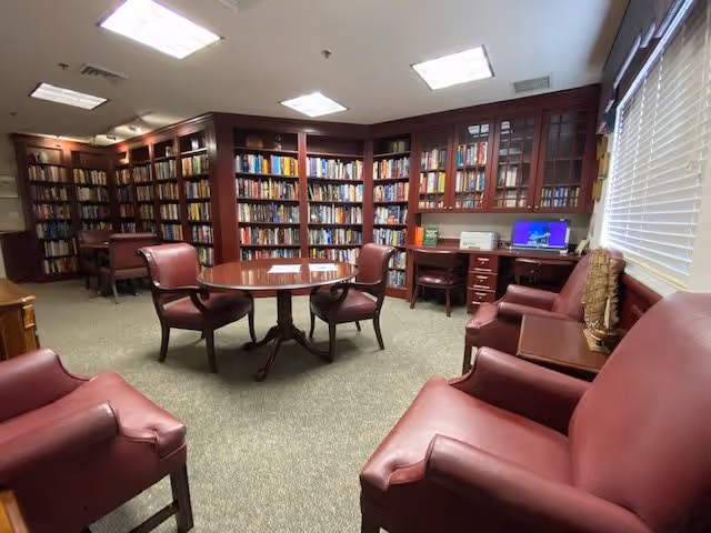 A cozy library/reading room with built-in bookshelves, a round table, and red leather chairs.
