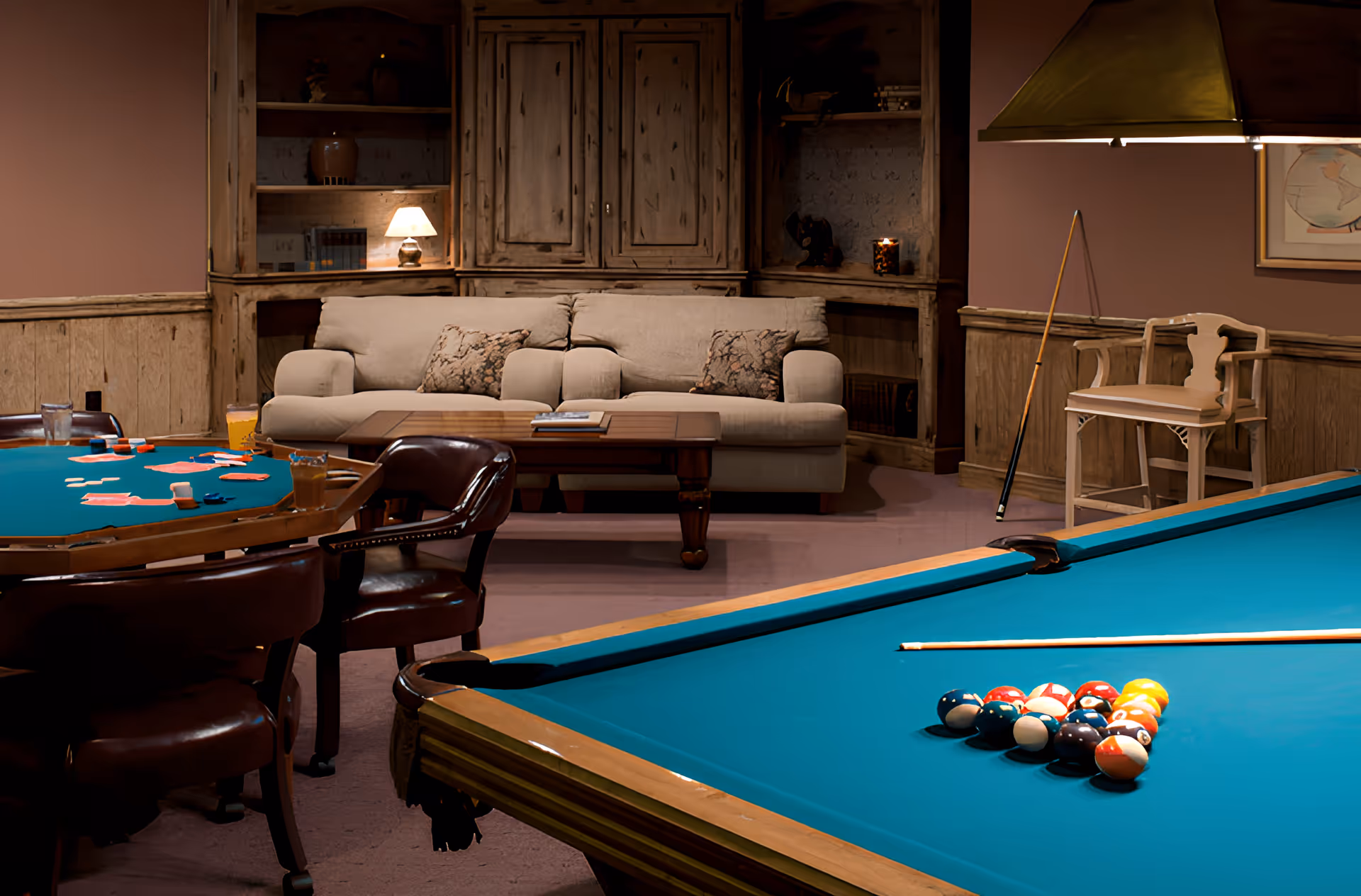 Game room with a pool table and racked billiard balls, a card table, and a sofa in front of wooden cabinets.