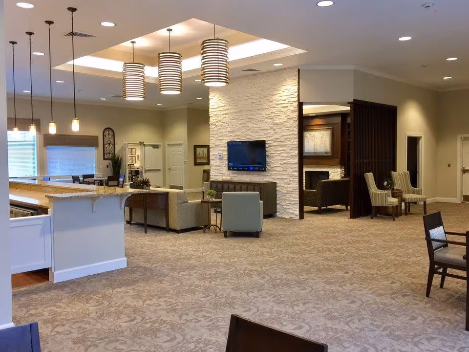 Spacious furnished common living area with seating, a TV mounted on a stone accent wall, pendant lights, and a kitchenette counter.
