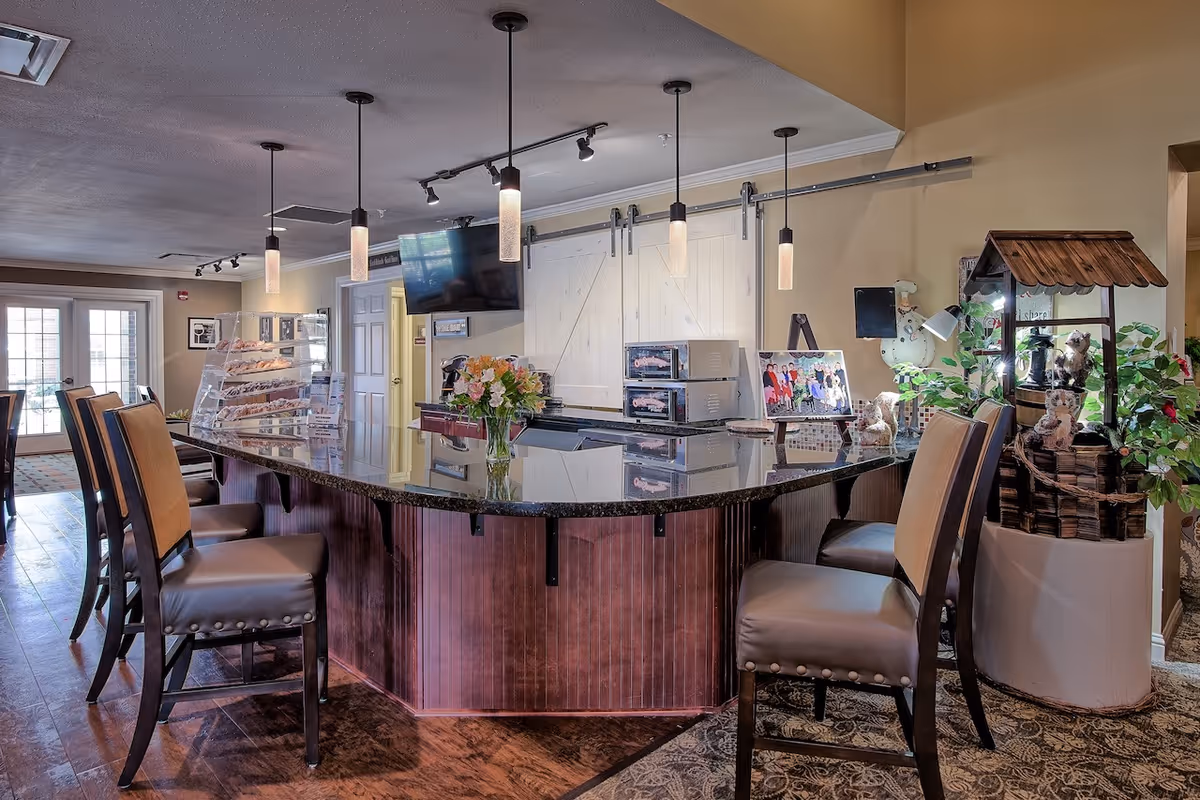 Interior communal dining/bar area with a curved granite-top counter, barstools, pendant lights, TV, and snack displays.