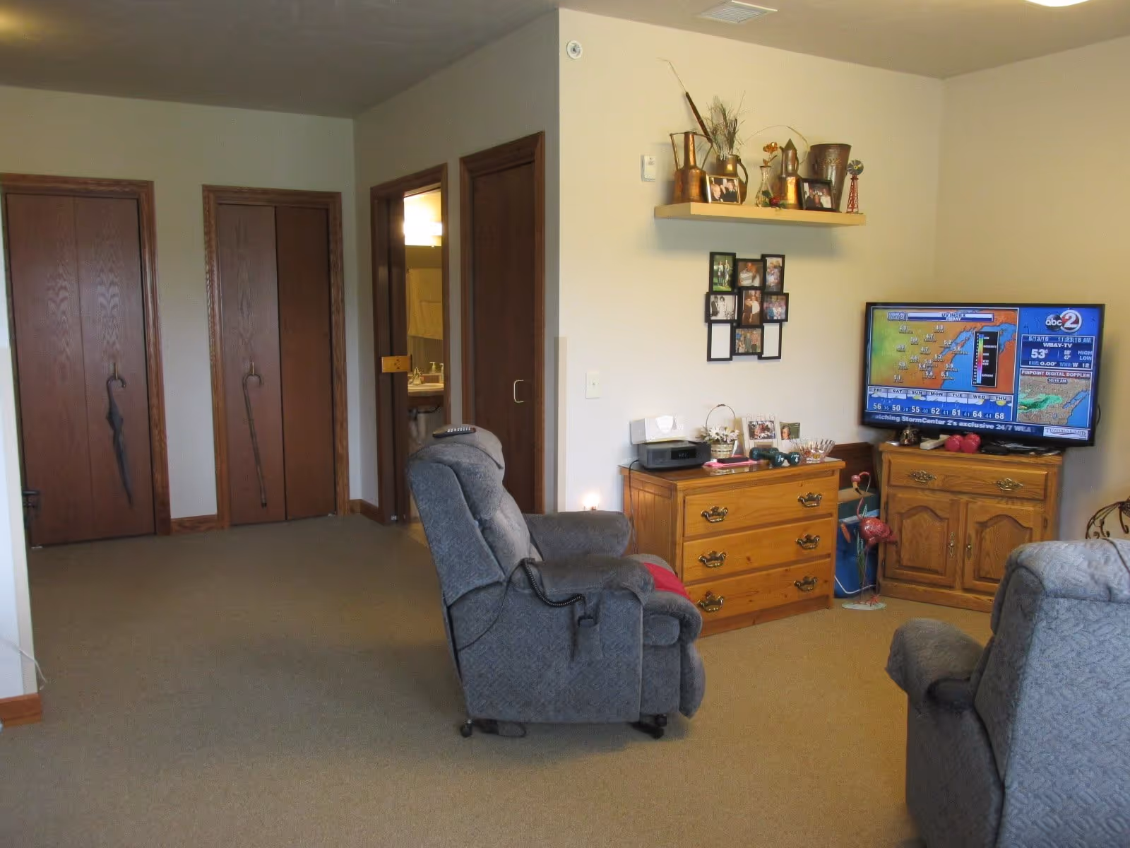 Living room with two gray recliners facing a TV on a wooden cabinet, dressers, and framed photos on the wall.