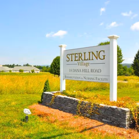 Sterling Village outdoor sign on a stone planter under a blue sky.