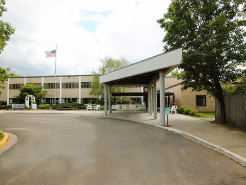 Exterior view of Langton Place facility with driveway, covered entrance, flagpole, and trees.