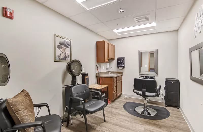 Small hair salon room with a styling chair, sink, cabinets, and waiting chairs.