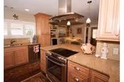 Bright traditional kitchen with a central island cooktop, wood cabinets, pendant lights, and decorative accents.