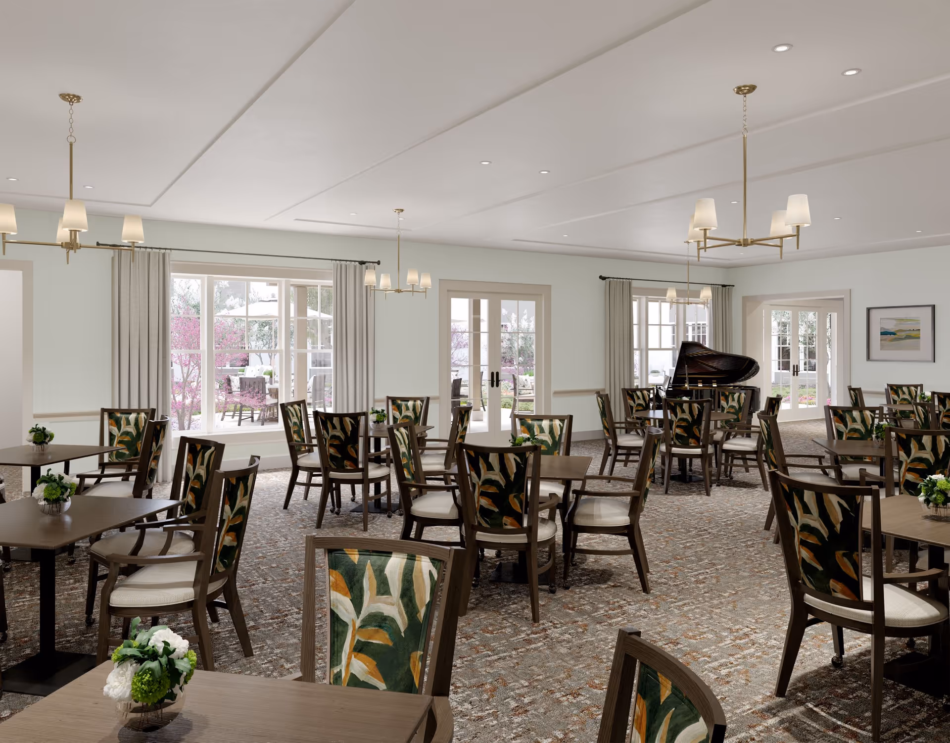 A spacious dining room with multiple wooden tables and chairs featuring green and orange patterned upholstery. The room has large windows and glass doors letting in natural light and offering a view of an outdoor patio with seating and greenery. There are chandeliers hanging from the ceiling and a grand piano in the corner.