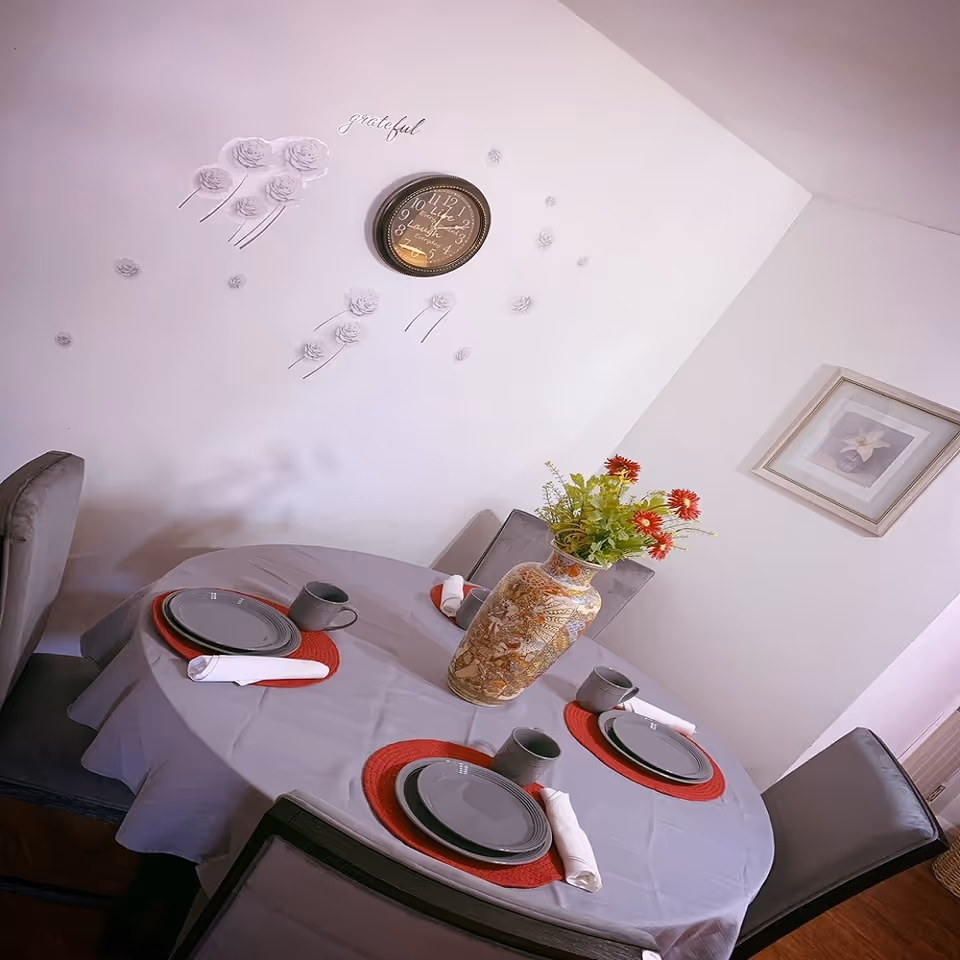 Round dining table with place settings and a floral vase in a softly decorated dining room.