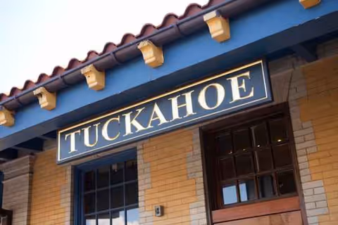 Exterior view of a brick building with a blue 'TUCKAHOE' sign above the entrance.