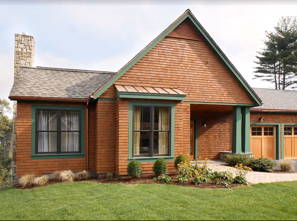 Front exterior of a single-story craftsman-style house with cedar shingle siding, green trim, a garage, and a landscaped lawn.