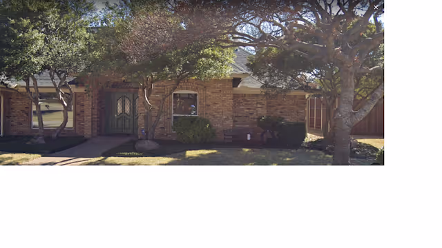 Exterior view of a single-story brick building with a green double front door, surrounded by trees and bushes, with a small pathway leading to the entrance.