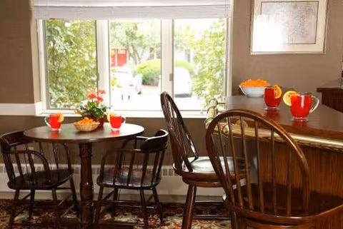 Sunlit dining area with a round table, chairs, and a kitchen counter by windows.