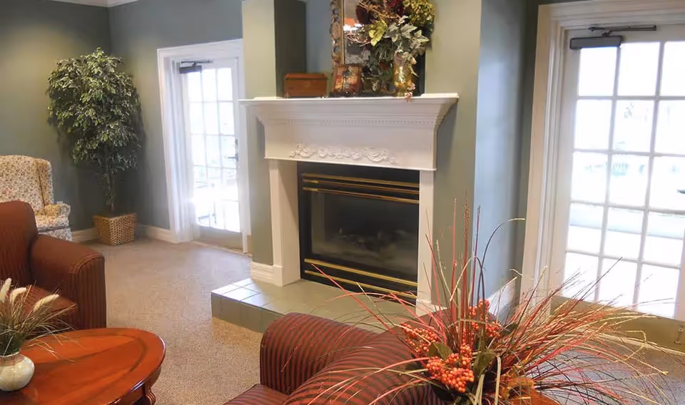 Cozy living room with a white mantel fireplace, striped armchairs, a coffee table and decorative plants by French doors.
