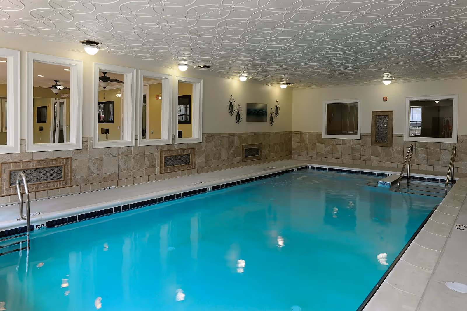 Indoor swimming pool with a tiled deck and windows looking into adjacent rooms.