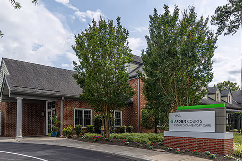 Exterior view of Arden Courts Virginia Beach facility with brick building, trees, and a sign.
