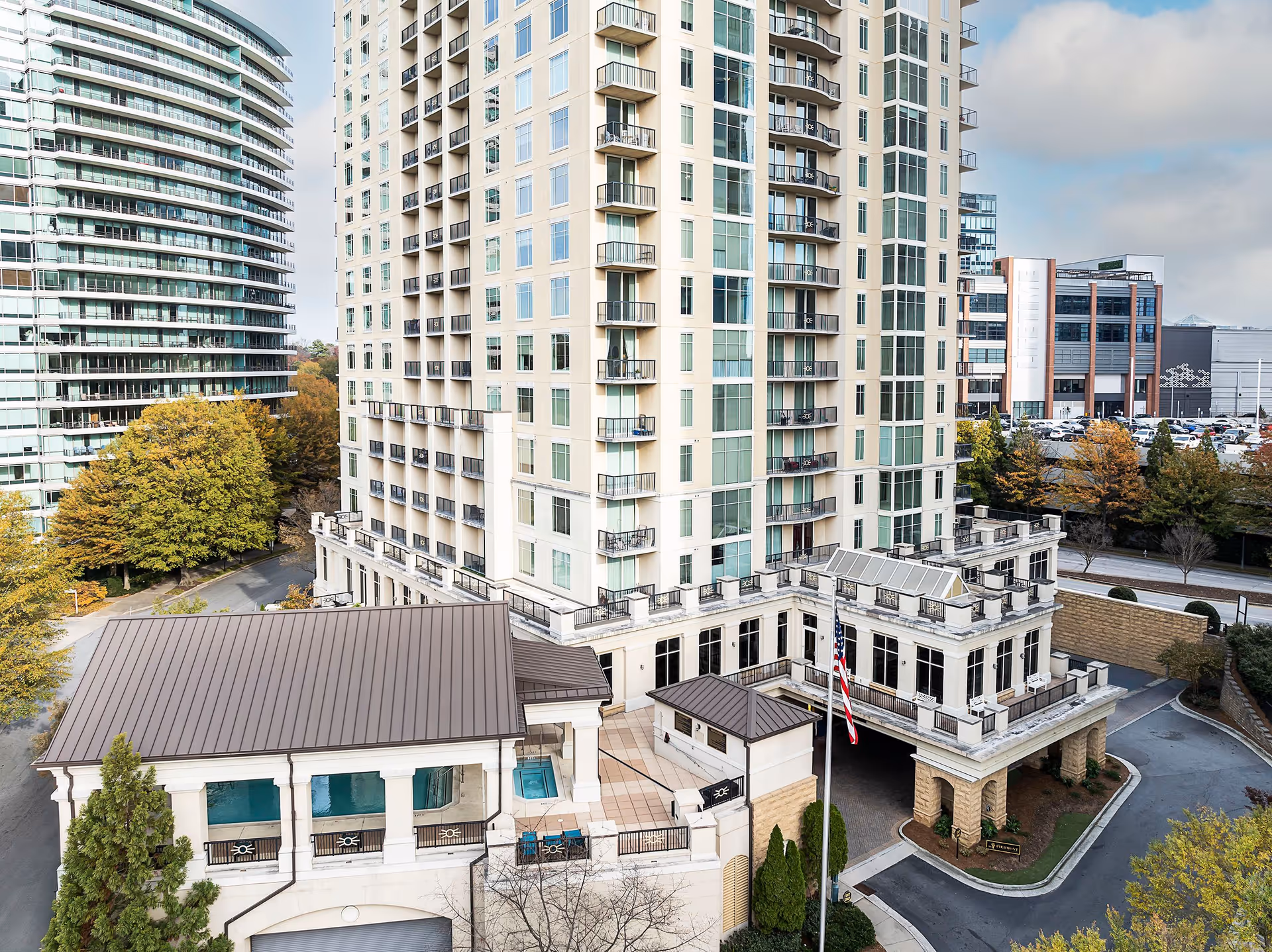 Exterior view of a multi-story residential tower with balconies, a porte-cochère entrance, and surrounding buildings and trees.