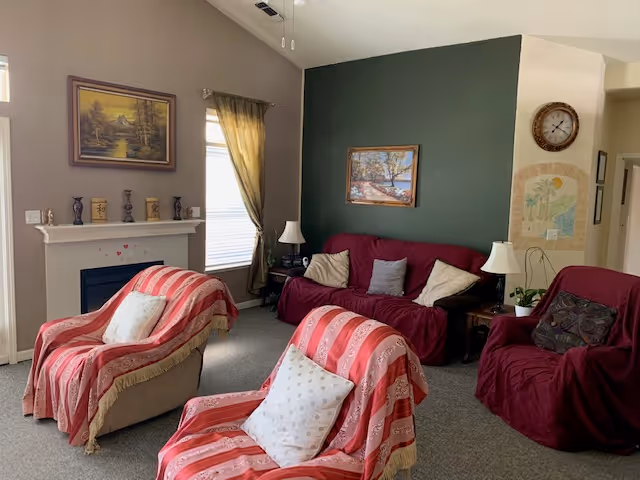 Cozy living room with sofas and armchairs draped in red throws, a fireplace, lamps, framed artwork, and a green accent wall.