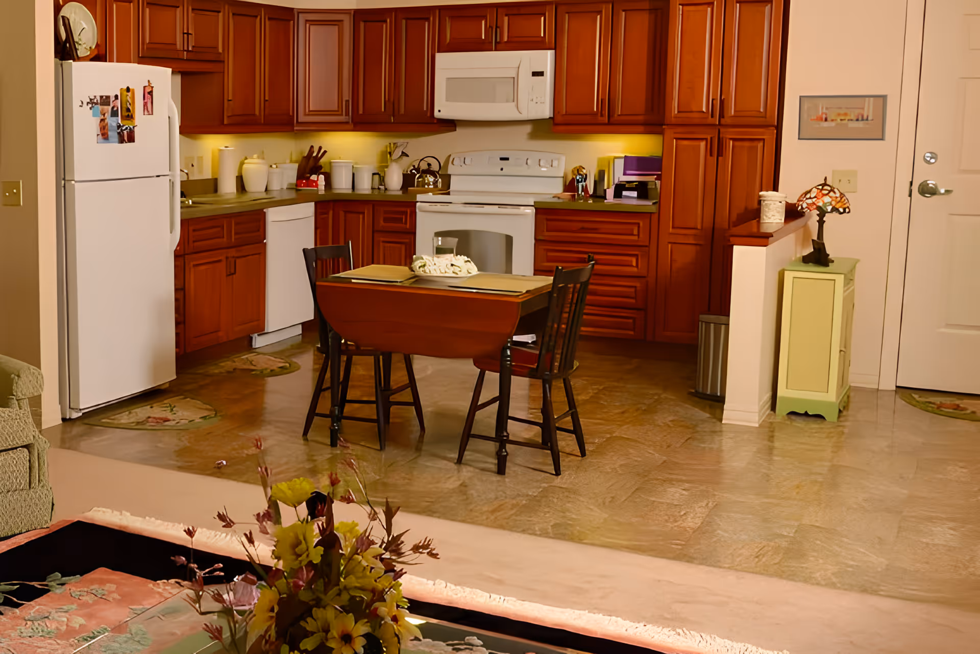 Open-plan kitchen with wooden cabinets, white appliances and a small dining table with two chairs