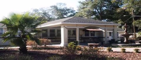 Front exterior of Her Heart Gardens Assisted Living, with a porch, palm tree, and fountain.